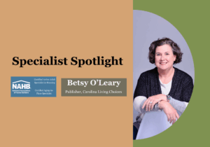 Betsy O'Leary, Aging in Place Specialist and Certified Active Adult Specialist in Housing, smiling at her desk, featured in a blog article about retirement.