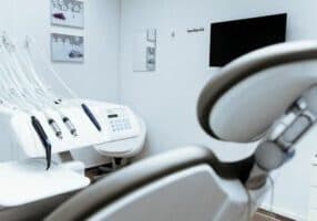 The dental office in Hendersonville features an empty patient chair, dental instruments, and a monitor on the wall. The room boasts white walls adorned with small artworks, creating a serene environment ideal for those approaching retirement.