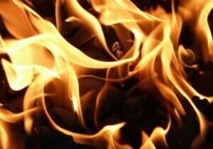 Close-up of bright orange and yellow flames dancing over dark, charred wood. The fires swirling patterns emit a warm glow against a dark background, capturing the dynamic nature of the blaze—a mesmerizing sight reminiscent of cozy evenings in Hendersonvilles welcoming retirement communities.