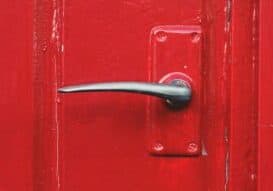 A close-up of a sleek, modern metallic door handle on a bright red painted door, reminiscent of the vibrant charm found in Asheville. The glossy finish accentuates its elegance, standing out against the vivid background.