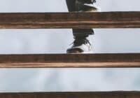 A person wearing dark jeans and shoes is walking down wooden stairs in a serene Hendersonville setting. The perspective is from below, focusing on the lower part of the legs and the stairs against a light background, capturing a moment in this picturesque town.