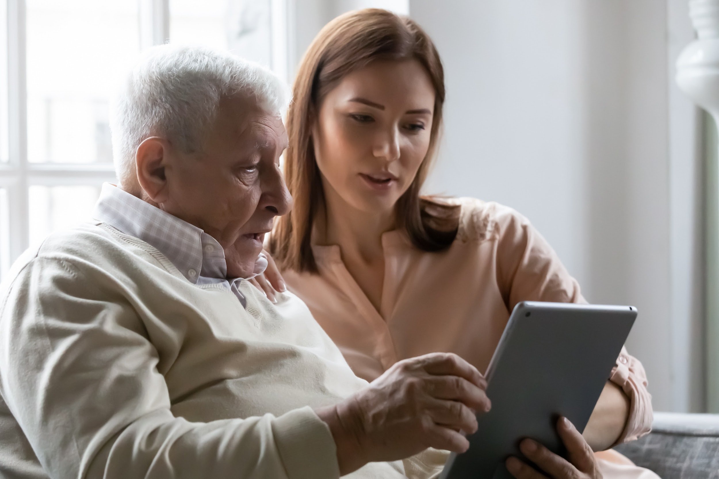 An elderly person is sitting comfortably in their own home, using a tablet for a telehealth consultation with a doctor. This scene highlights the importance of home care services for older adults, allowing them to maintain their independence while receiving necessary health support.