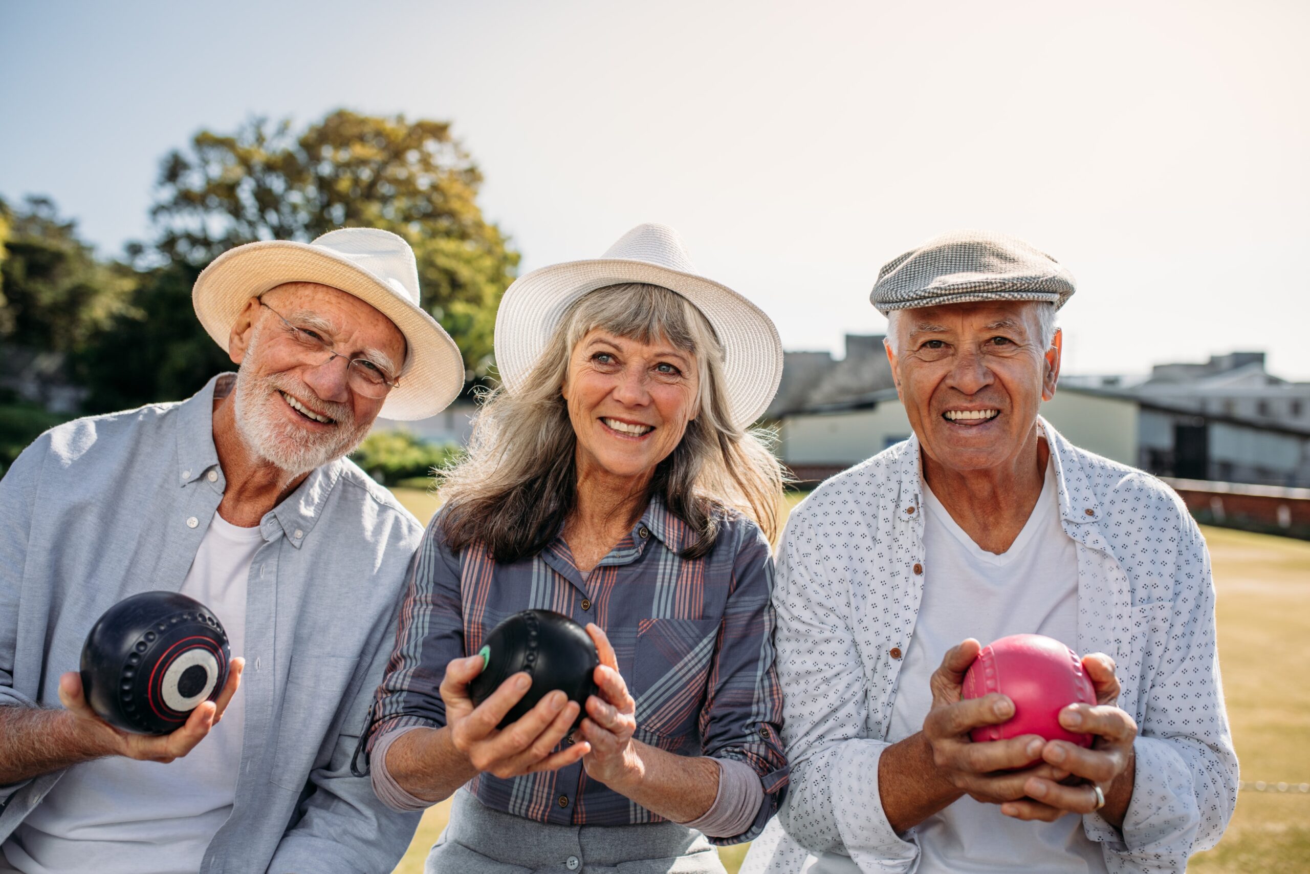 Two men and a woman holding balls while enjoying the outdoors