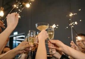 A group of people raise champagne glasses in a celebratory toast, surrounded by sparklers. The scene is festive with a dimly lit background, highlighting the sparkling lights and bubbles in the glasses, as they joyfully celebrate a retirement in Asheville.