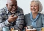 Retirement Community Gathering Around a Table to Eat Pound Cake A group of older adults sit around a table, smiling and laughing together while enjoying coffee, cake, and pastries in a bright, cozy setting.